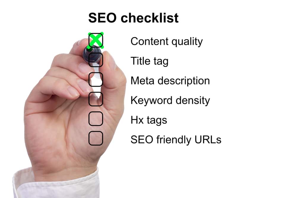 Hand with a marker ticking off items on an SEO checklist including content quality and keyword density.