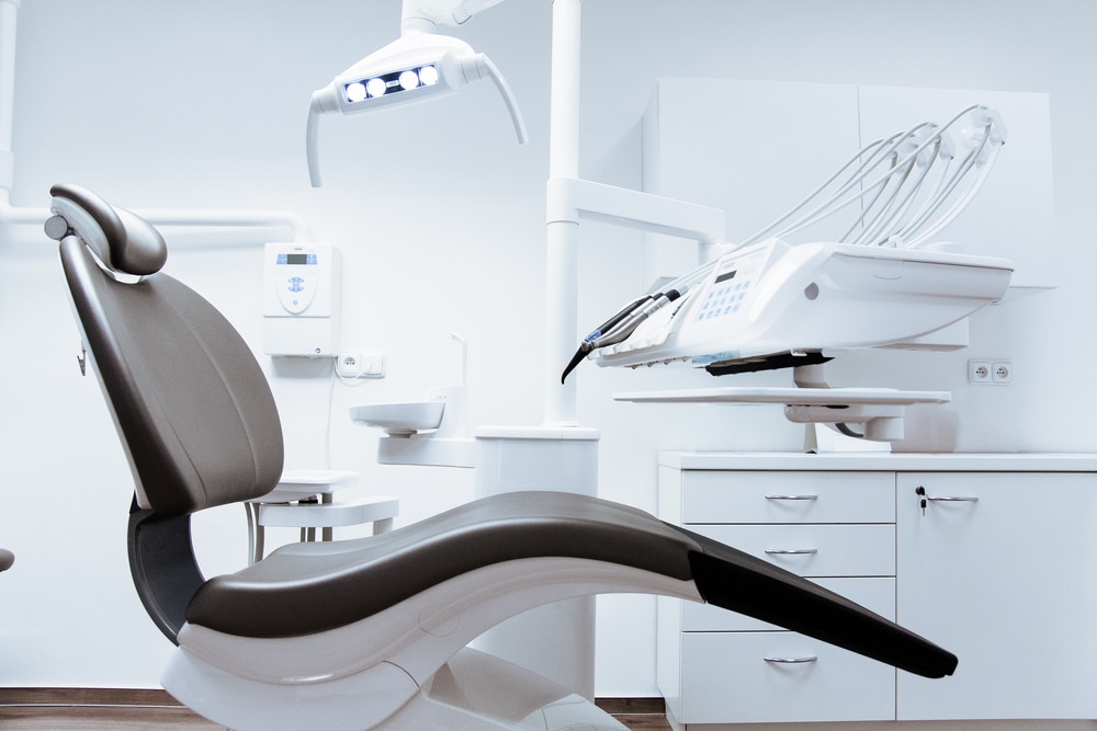  An empty modern dental operatory with a patient chair in focus and state-of-the-art equipment in a clean, white room.